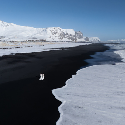 Iceland elopement photo with two brides on black sand beach by snowy mountains