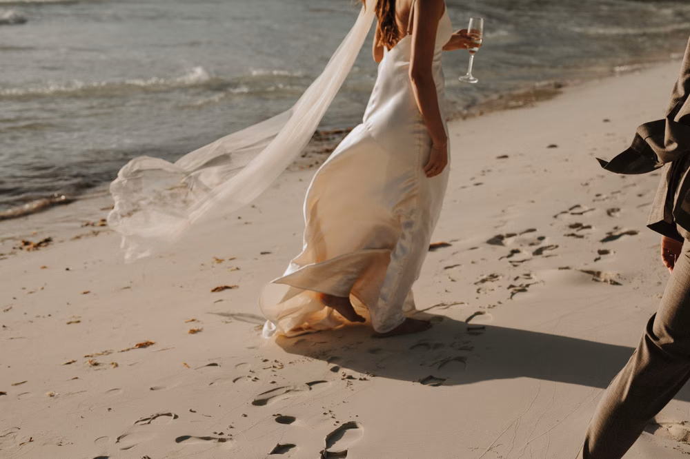 bride walking on beach with wine glass