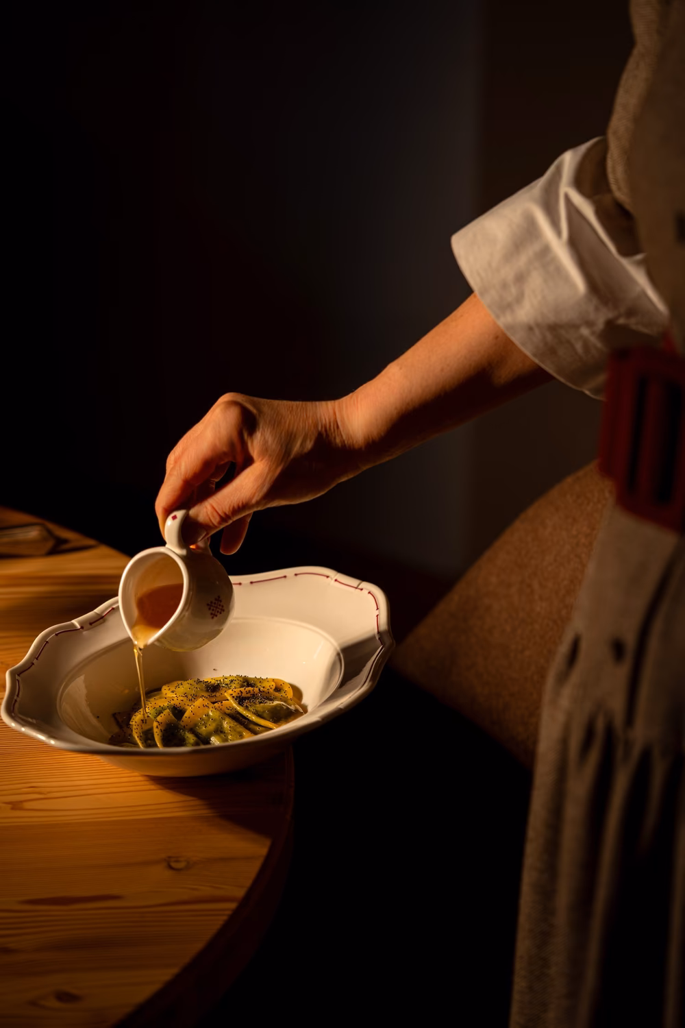 Server pouring sauce over a South Tyrolean pasta dish at a wooden table