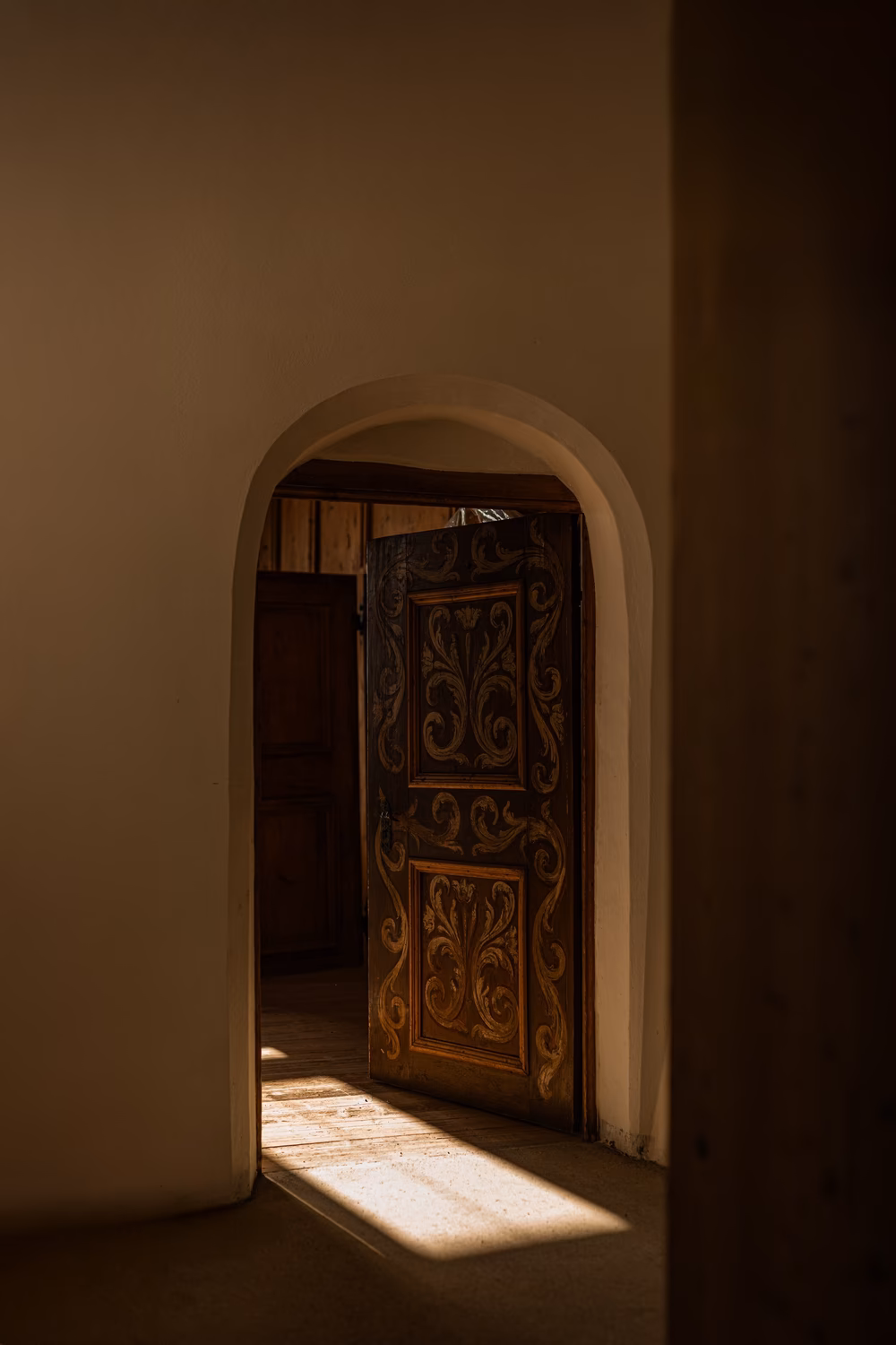 Sunlight falling through an arched doorway onto an ornately carved antique wooden door at Castel Badia