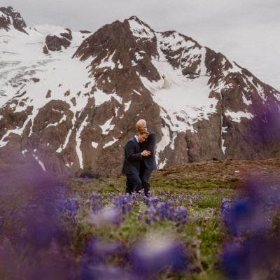 Gay destination wedding photo in Alaska with mountain backdrop and purple flowers
