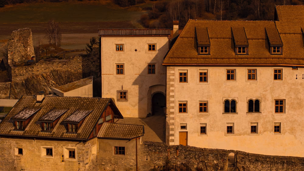 Cream stone exterior and shingled rooftops of Castel Badia castle hotel in the Dolomites at golden hour