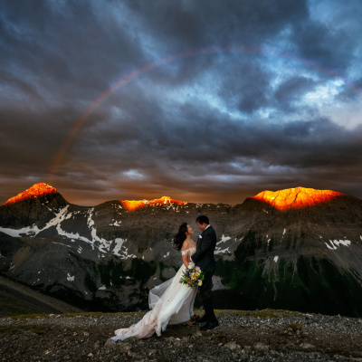 Dramatic destination wedding photo in the Canadian Rocky Mountains under a rainbow